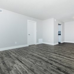 Large living room with plank flooring with a view of the kitchen at Carlson Apartments, located in Colorado Springs, CO